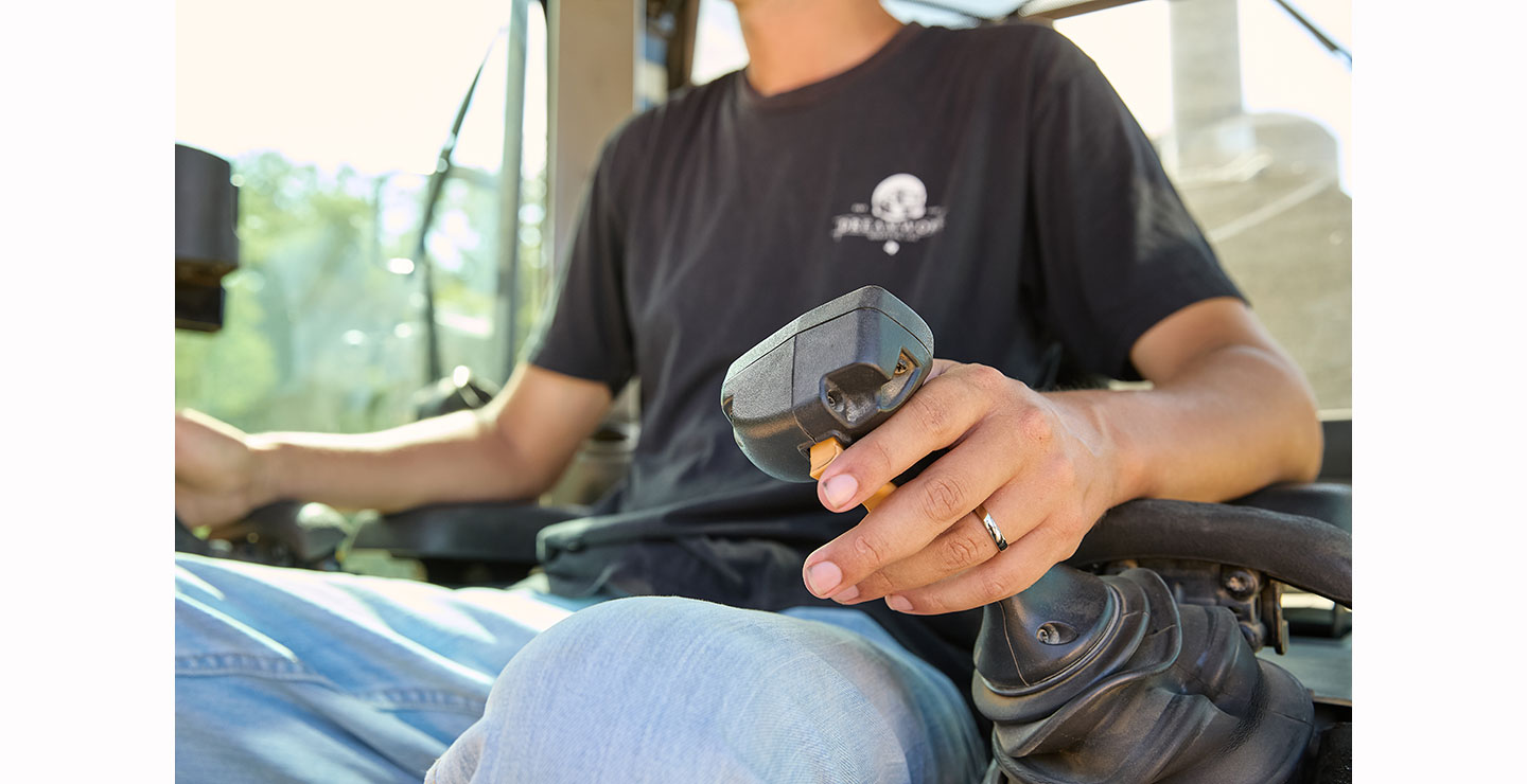 Close-up of a man, Nick Castillion, sitting in an equipment cab, holding a black control joystick with his left hand, wearing a black T-shirt and jeans.